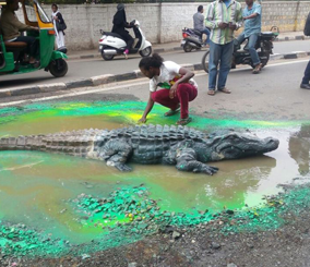 “بالصور” فنان هندي يضع تمساحاً ضخماً في حفرة بالمدينة لتنبيه المسؤولين حتى يشاهدونها